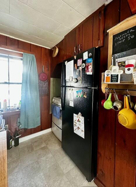 kitchen featuring black fridge, white electric range, and wooden walls