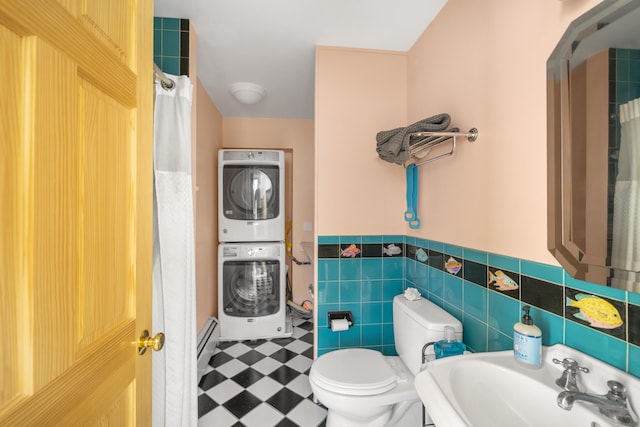 bathroom featuring sink, baseboard heating, tile walls, stacked washer / dryer, and toilet