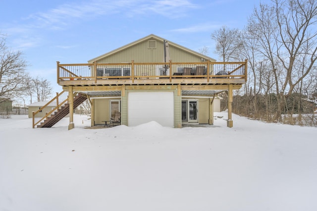 snow covered rear of property featuring a wooden deck and a garage