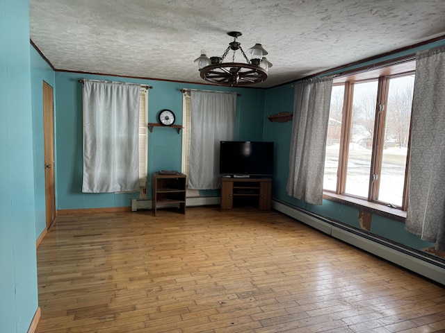 unfurnished living room with an inviting chandelier, a baseboard heating unit, and light wood-type flooring