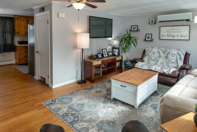 living room with a wall mounted air conditioner, ceiling fan, baseboard heating, crown molding, and light wood-type flooring