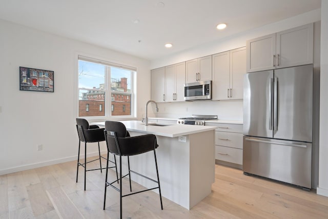 kitchen with a center island with sink, appliances with stainless steel finishes, a kitchen breakfast bar, light wood-style floors, and a sink