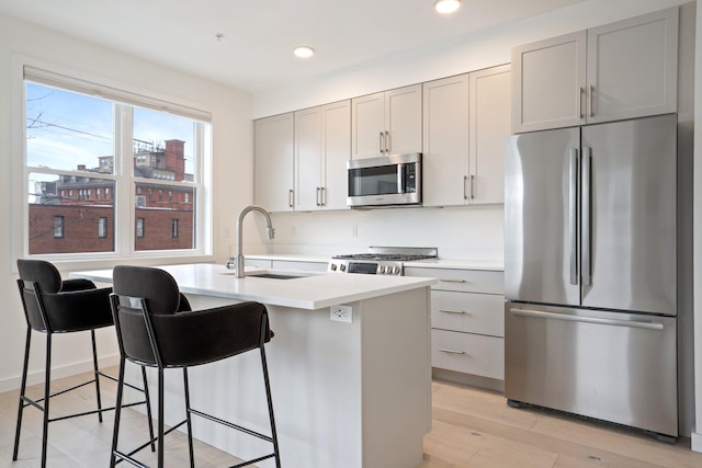 kitchen featuring a center island with sink, appliances with stainless steel finishes, light countertops, light wood-type flooring, and a sink