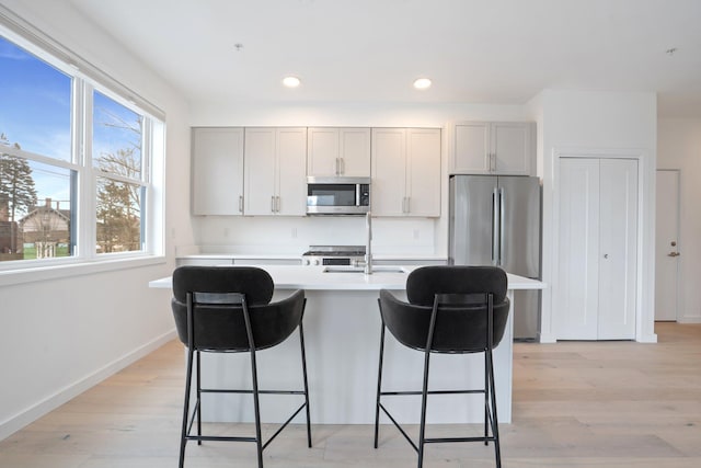 kitchen with a breakfast bar, light wood finished floors, light countertops, appliances with stainless steel finishes, and a kitchen island with sink