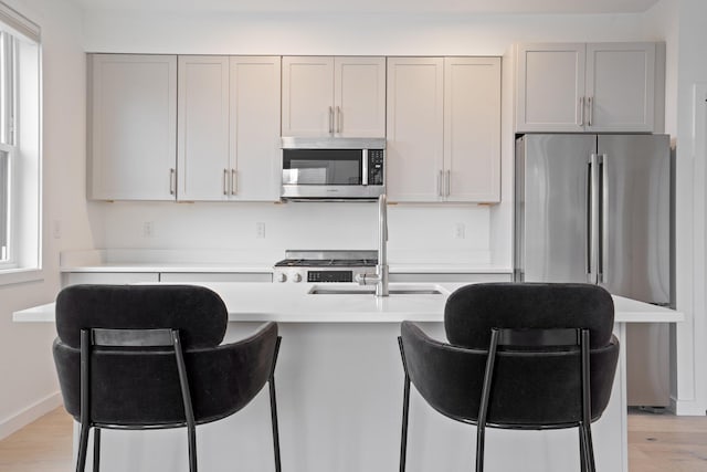 kitchen with appliances with stainless steel finishes, light countertops, light wood-style flooring, and a breakfast bar area