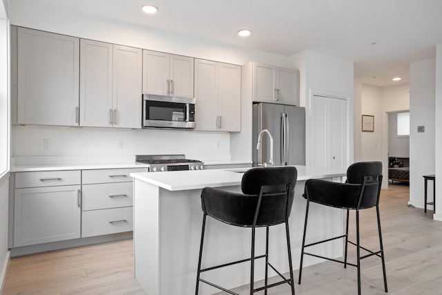 kitchen featuring light wood-type flooring, a breakfast bar area, stainless steel appliances, and light countertops