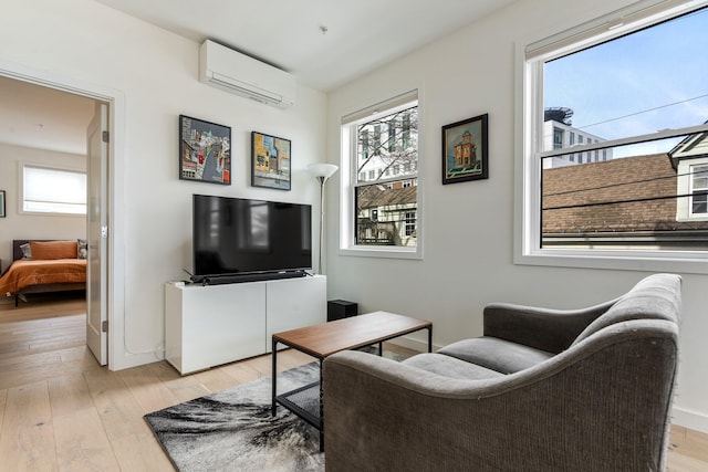 living room with a wall unit AC, a healthy amount of sunlight, baseboards, and light wood finished floors