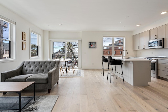 kitchen featuring a center island with sink, gray cabinets, appliances with stainless steel finishes, a sink, and light wood-type flooring