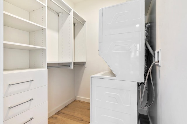 spacious closet with light wood-type flooring and stacked washing maching and dryer