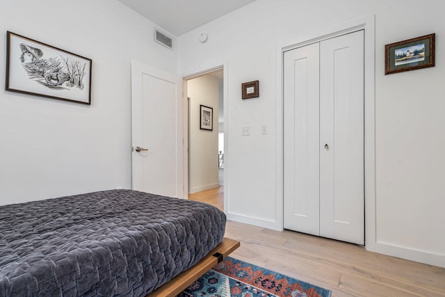 bedroom featuring light wood finished floors, a closet, visible vents, and baseboards