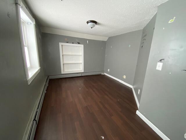 unfurnished room featuring built in shelves, dark hardwood / wood-style floors, a textured ceiling, and a baseboard heating unit