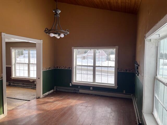 empty room featuring dark wood-type flooring, baseboard heating, an inviting chandelier, high vaulted ceiling, and wooden ceiling