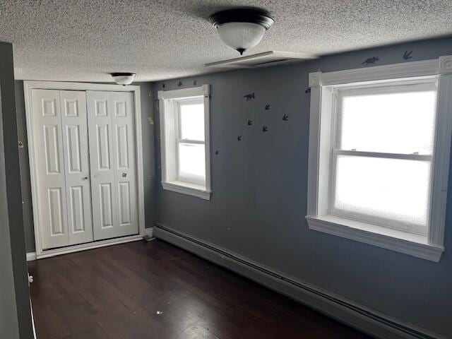 unfurnished bedroom featuring dark wood-type flooring, a closet, a textured ceiling, and baseboard heating