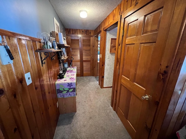 hallway featuring light colored carpet, a textured ceiling, and wood walls