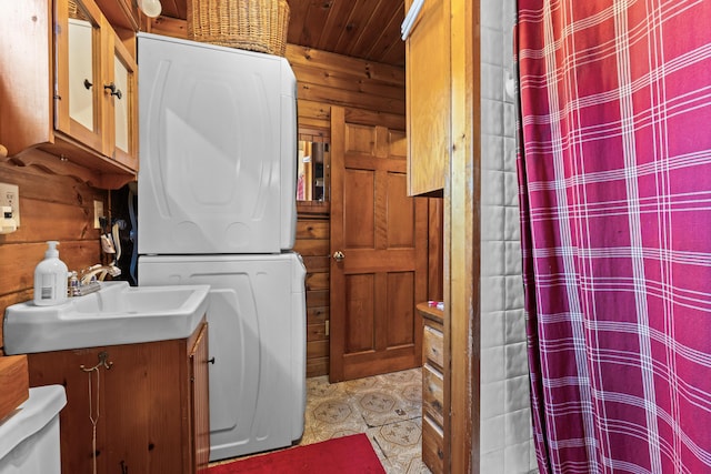 laundry room with stacked washer and clothes dryer, sink, and wood walls