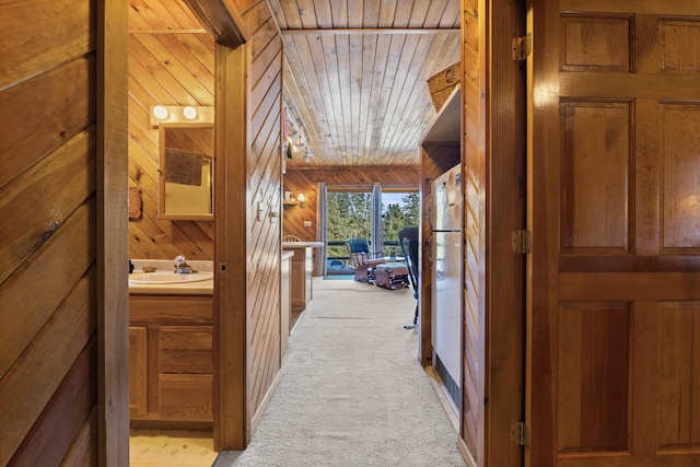 hallway with sink, light colored carpet, wood ceiling, and wood walls