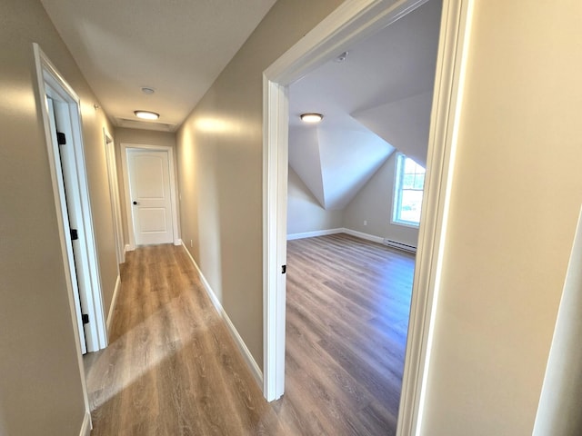 hall with a baseboard radiator, lofted ceiling, and light wood-type flooring