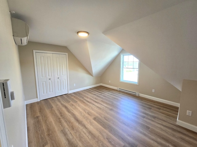 bonus room featuring hardwood / wood-style floors, a wall mounted air conditioner, vaulted ceiling, and baseboard heating