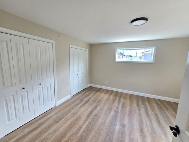 unfurnished bedroom with light hardwood / wood-style flooring and multiple closets