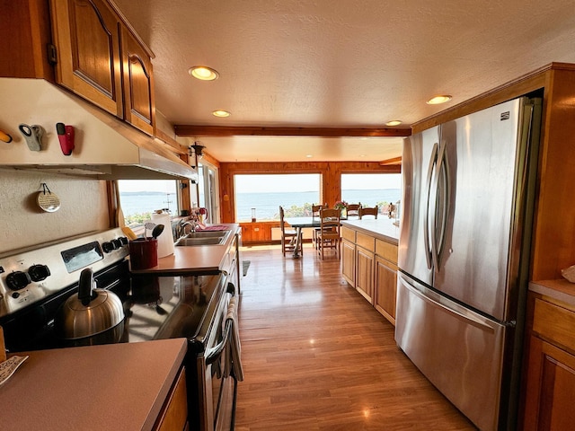 kitchen featuring appliances with stainless steel finishes, sink, light hardwood / wood-style floors, a water view, and a textured ceiling