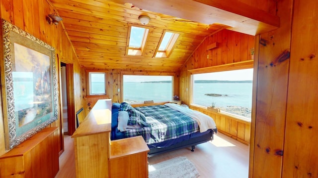 bedroom featuring multiple windows, wood walls, vaulted ceiling with skylight, and a water view