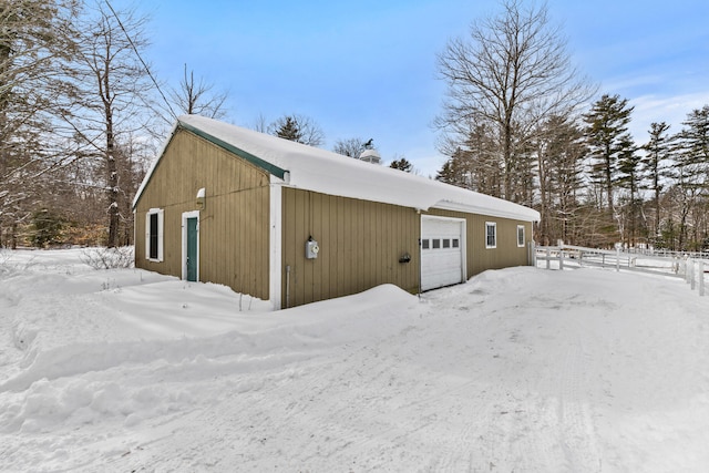 snow covered garage with a garage and fence