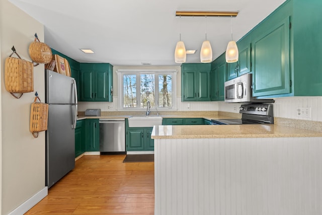 kitchen featuring a peninsula, a sink, light countertops, appliances with stainless steel finishes, and light wood-type flooring