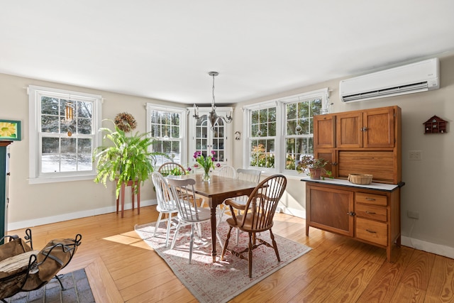 dining area with a chandelier, light wood finished floors, a wall unit AC, and baseboards