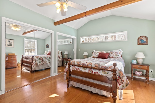 bedroom featuring vaulted ceiling with beams, ceiling fan, wood finished floors, and two closets