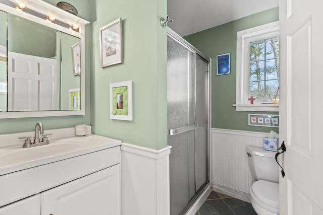 full bath featuring toilet, a wainscoted wall, vanity, tile patterned floors, and a stall shower