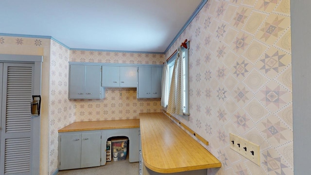 kitchen featuring light countertops, ornamental molding, blue cabinetry, and wallpapered walls