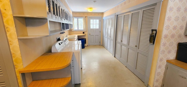 interior space featuring concrete flooring, washing machine and dryer, a sink, open shelves, and wallpapered walls