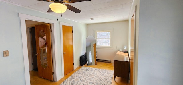 corridor with light wood finished floors and a baseboard heating unit