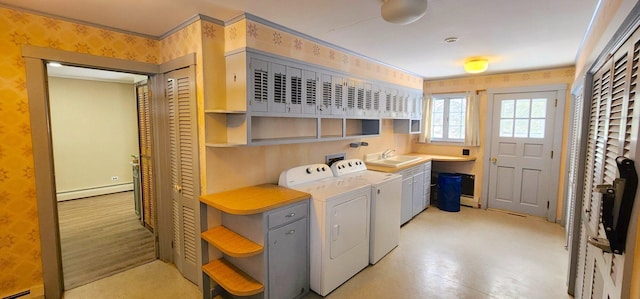 laundry room featuring cabinet space, wallpapered walls, a baseboard radiator, washing machine and clothes dryer, and a sink