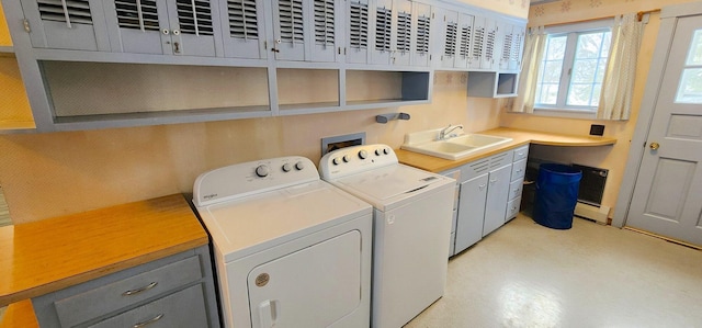 clothes washing area with separate washer and dryer, baseboard heating, a sink, and cabinet space