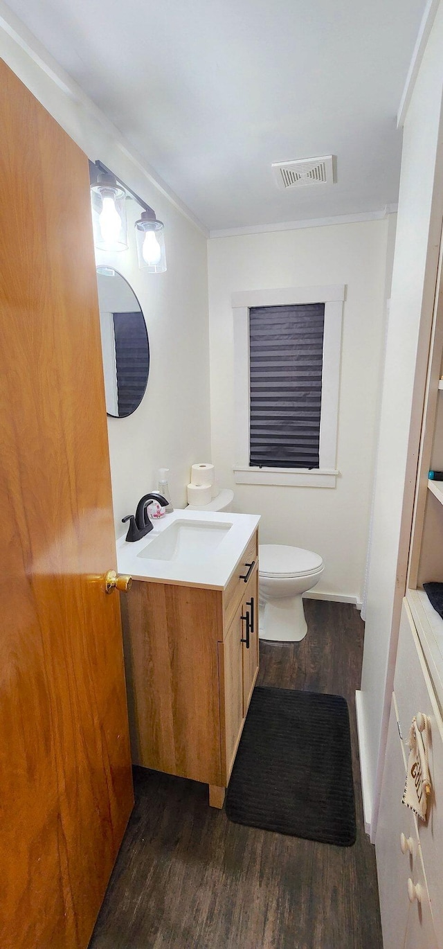 bathroom with toilet, wood finished floors, visible vents, vanity, and crown molding