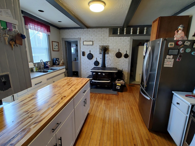 kitchen with butcher block countertops, sink, white cabinets, and a wood stove