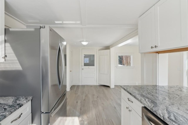 kitchen with appliances with stainless steel finishes, white cabinets, light stone counters, and light wood finished floors