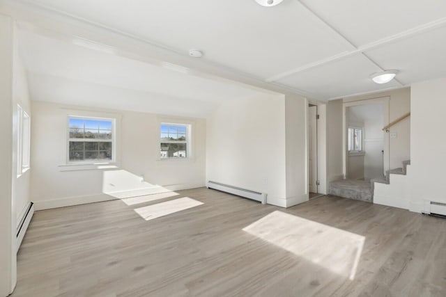 spare room featuring a baseboard heating unit, light wood-type flooring, and stairs