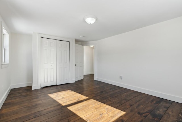 unfurnished bedroom with a closet, dark wood finished floors, and baseboards