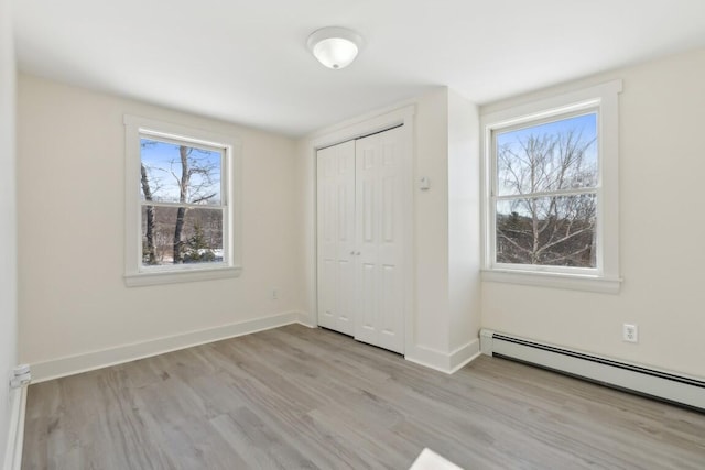 unfurnished bedroom with a baseboard heating unit, a closet, wood finished floors, and baseboards