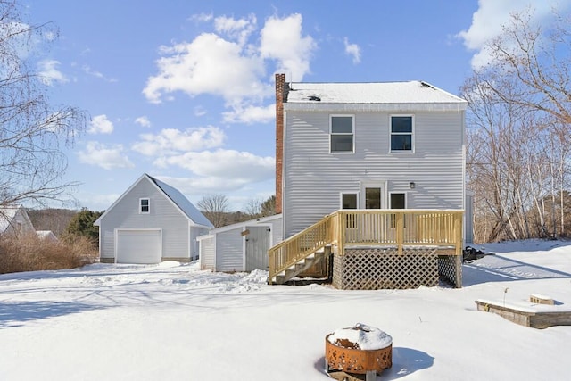 snow covered back of property with a garage, a deck, stairway, and an outdoor structure