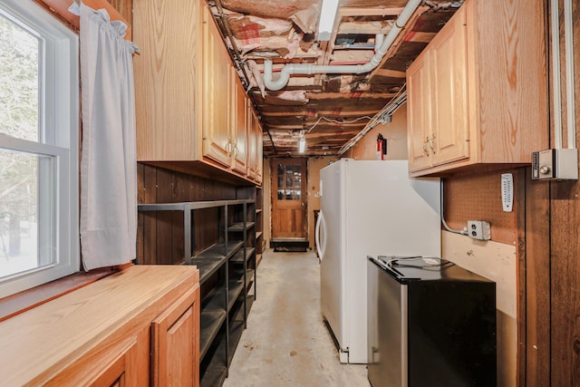 kitchen with unfinished concrete floors, freestanding refrigerator, light countertops, a healthy amount of sunlight, and light brown cabinets