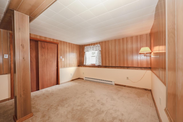 spare room with baseboards, light colored carpet, wood walls, and baseboard heating