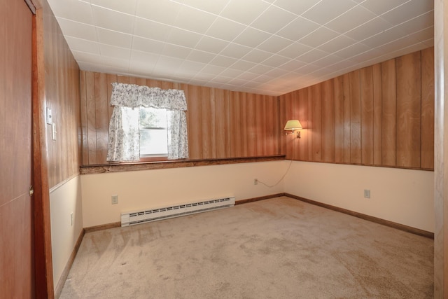 spare room featuring light carpet, baseboards, wooden walls, and a baseboard heating unit