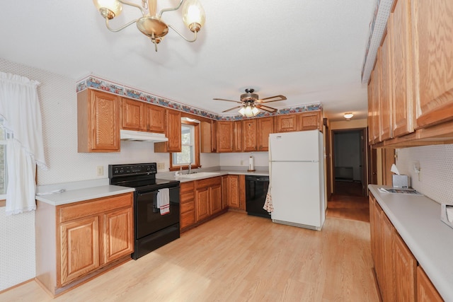 kitchen with brown cabinetry, under cabinet range hood, light countertops, black appliances, and a sink