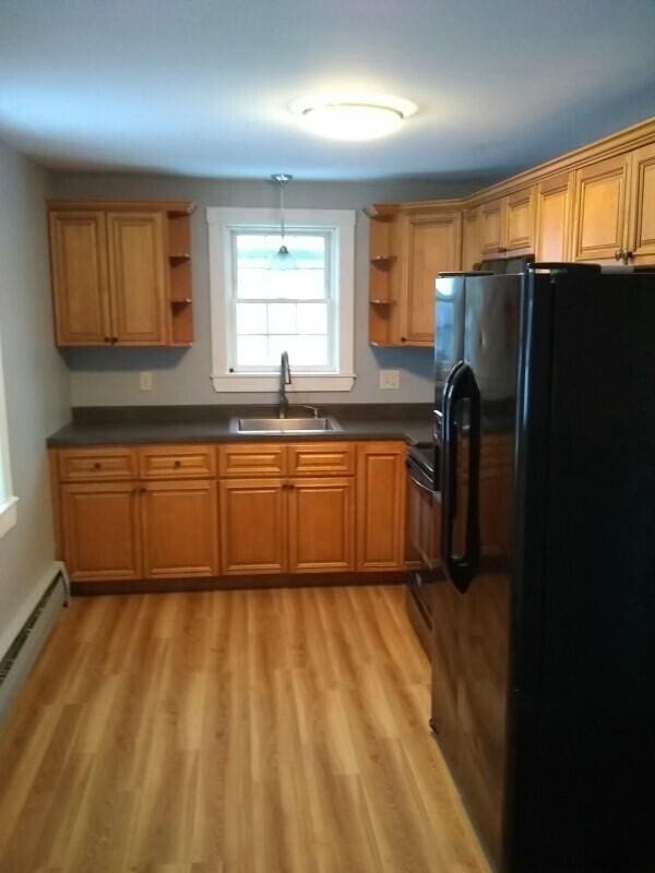 kitchen featuring a baseboard radiator, sink, black refrigerator with ice dispenser, and light wood-type flooring