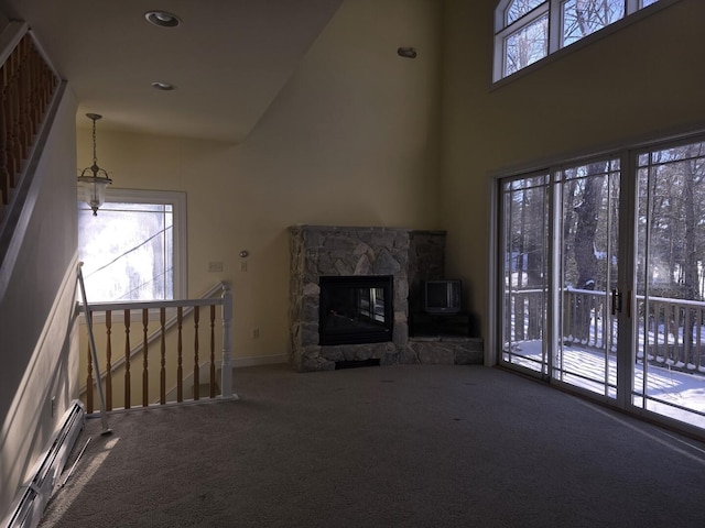 unfurnished living room with a baseboard radiator, plenty of natural light, a stone fireplace, and carpet