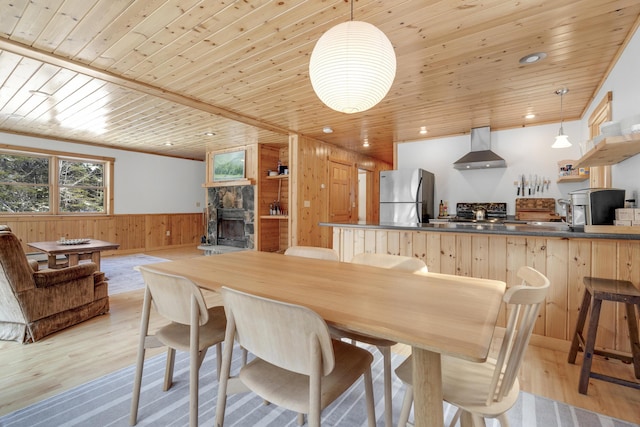 dining room featuring a stone fireplace, wooden walls, wooden ceiling, and light hardwood / wood-style floors