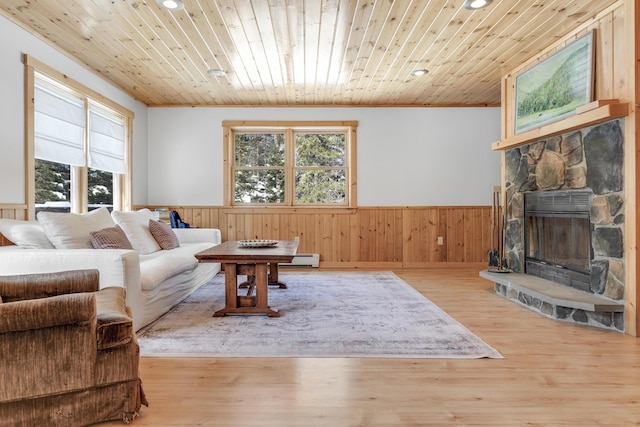 living room with wood ceiling, baseboard heating, ornamental molding, a stone fireplace, and light wood-type flooring